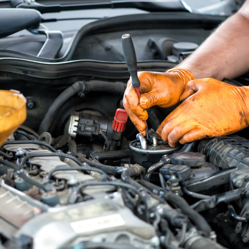 A close-up of hands working underneath the hood of a car.